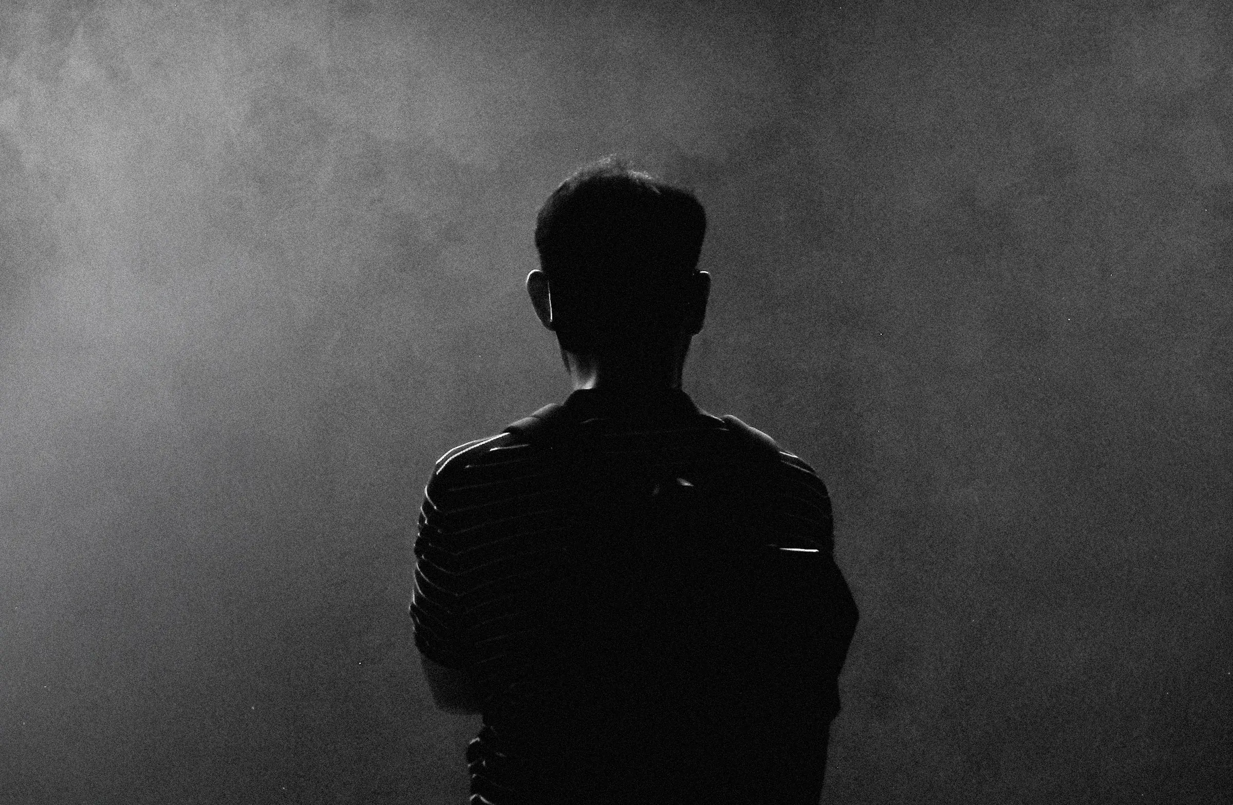 A figure seen from behind, silhouetted against drifting smoke