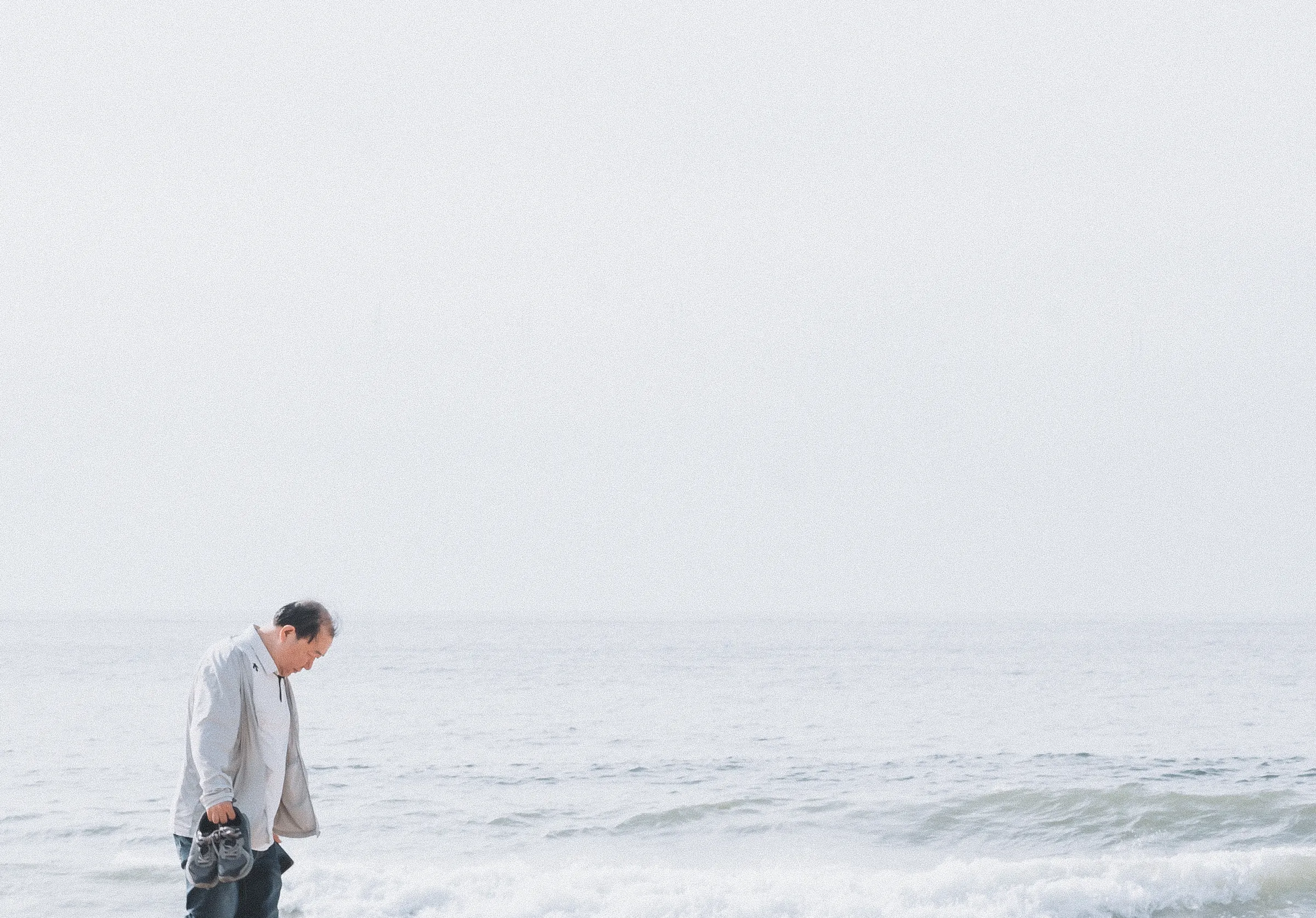 A man walking along the shoreline, holding his shoes